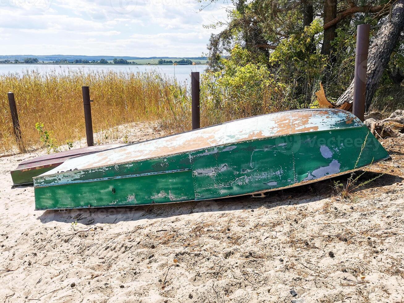 Abandoned green wooden boat resting on sandy shore surrounded by tall grass and water photo