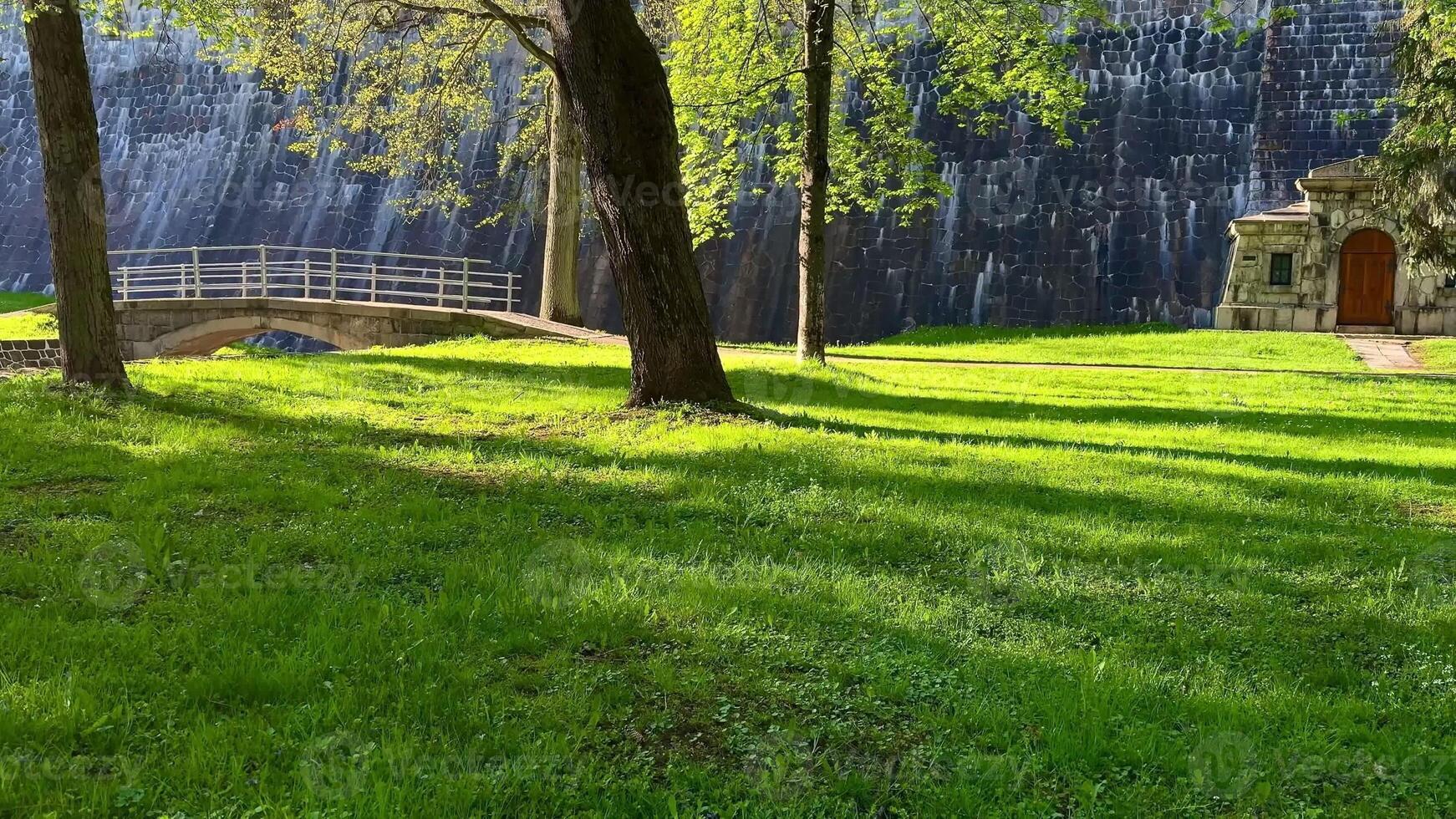 A tranquil park scene showcasing a charming stone structure, lush vibrant grass, and trees near a dam wall photo