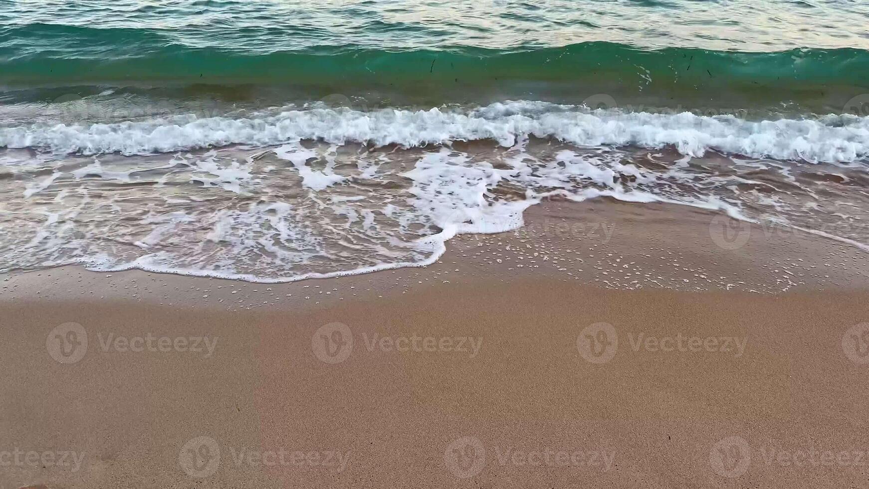 A beautiful beach scene characterized by gentle waves lapping against the warm sand, with a distant shoreline at sunset photo