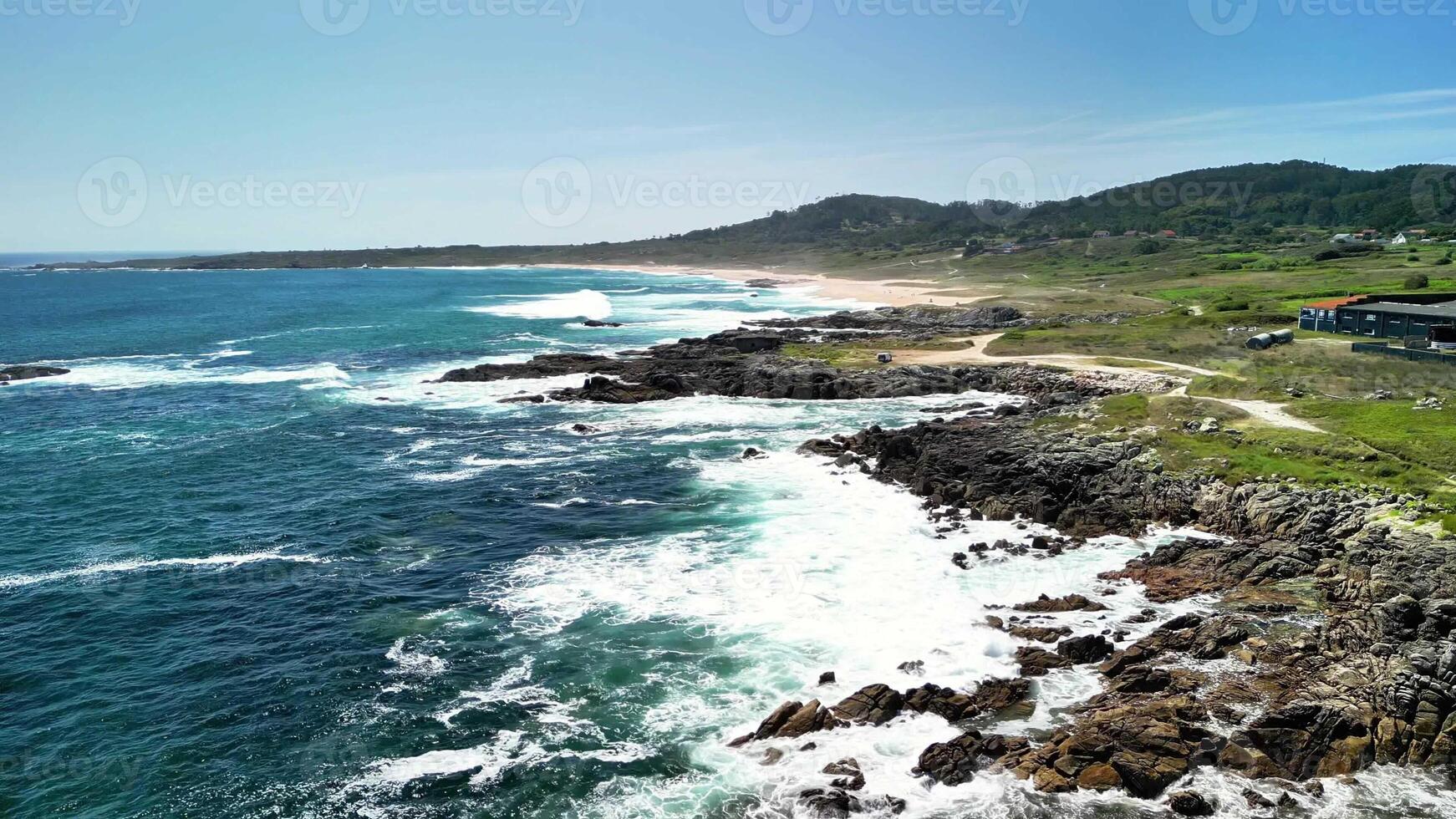 Capture the breathtaking beauty of the coast with waves dramatically crashing upon the rocky shores beneath clear skies photo