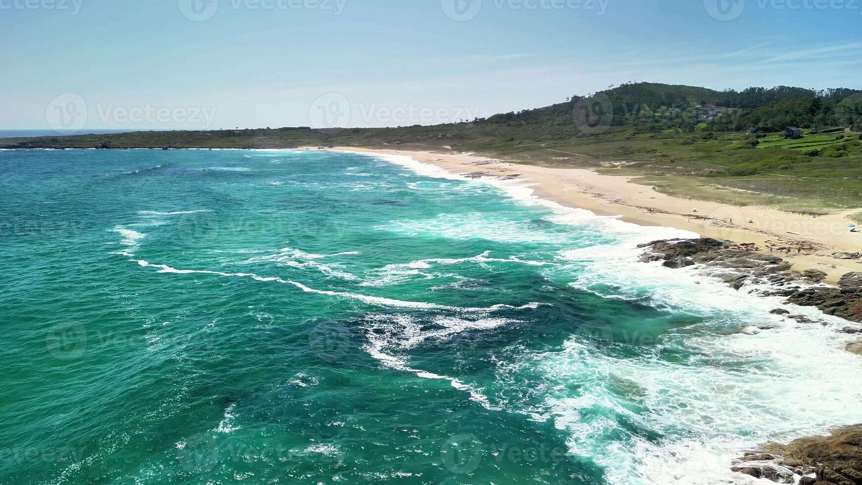 This aerial view showcases a stunning beach with crashing waves, golden sand, and lush green hills behind photo