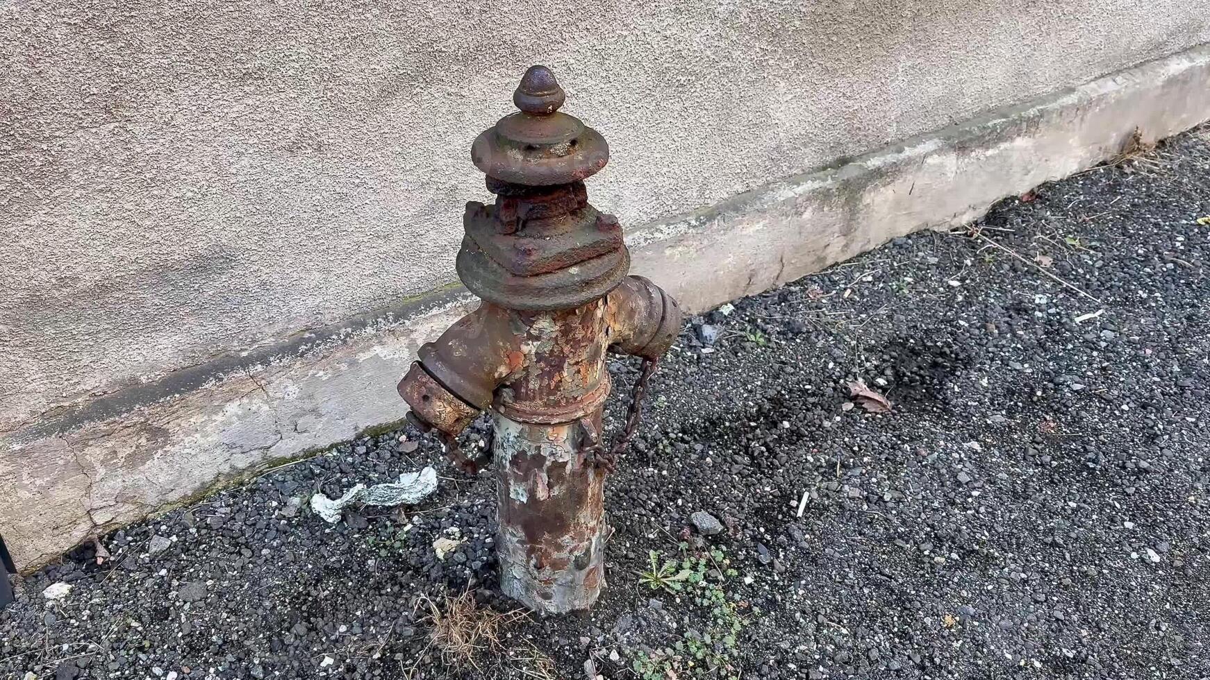 An old, weathered fire hydrant covered in rust and decay stands in stark contrast to the concrete wall behind it photo