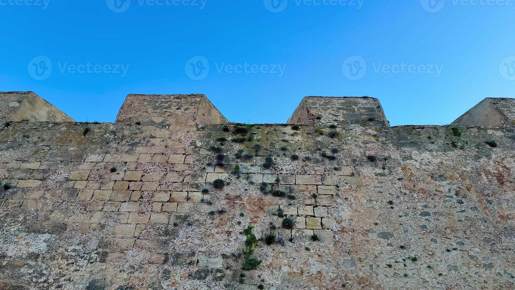 A detailed and immersive view of a weathered stone fortress wall set against a perfectly clear blue sky photo