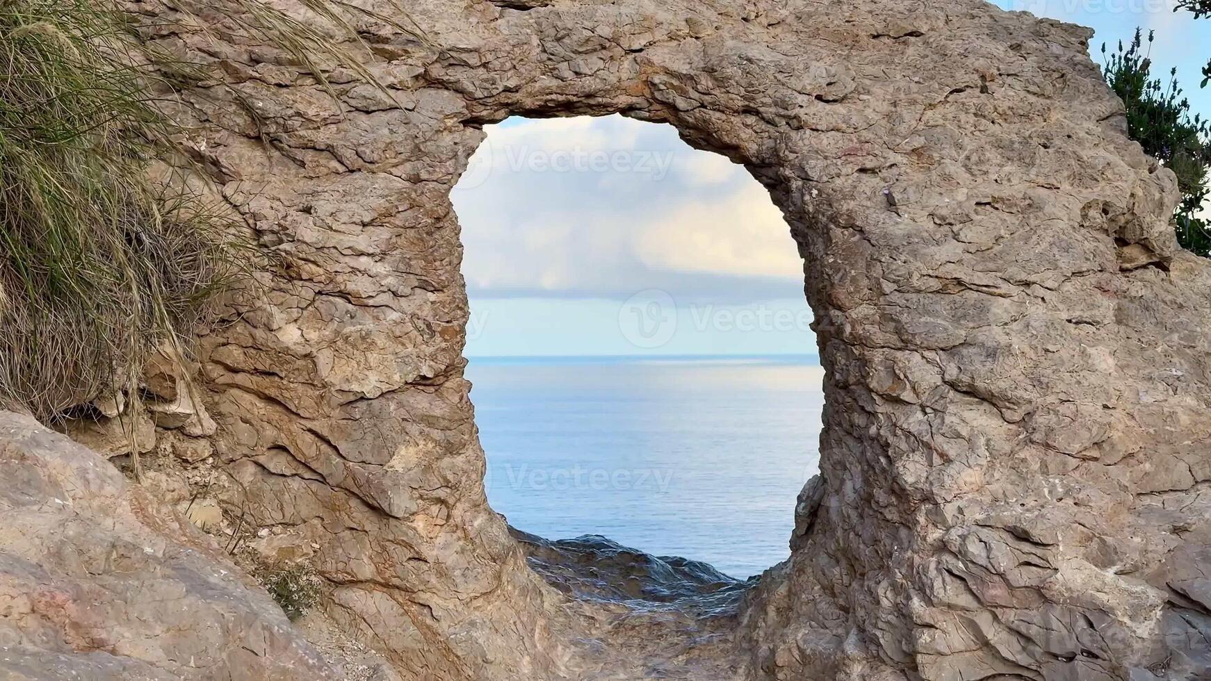 The stunningly beautiful view of the vast ocean is framed perfectly by a natural rock arch under clear skies photo