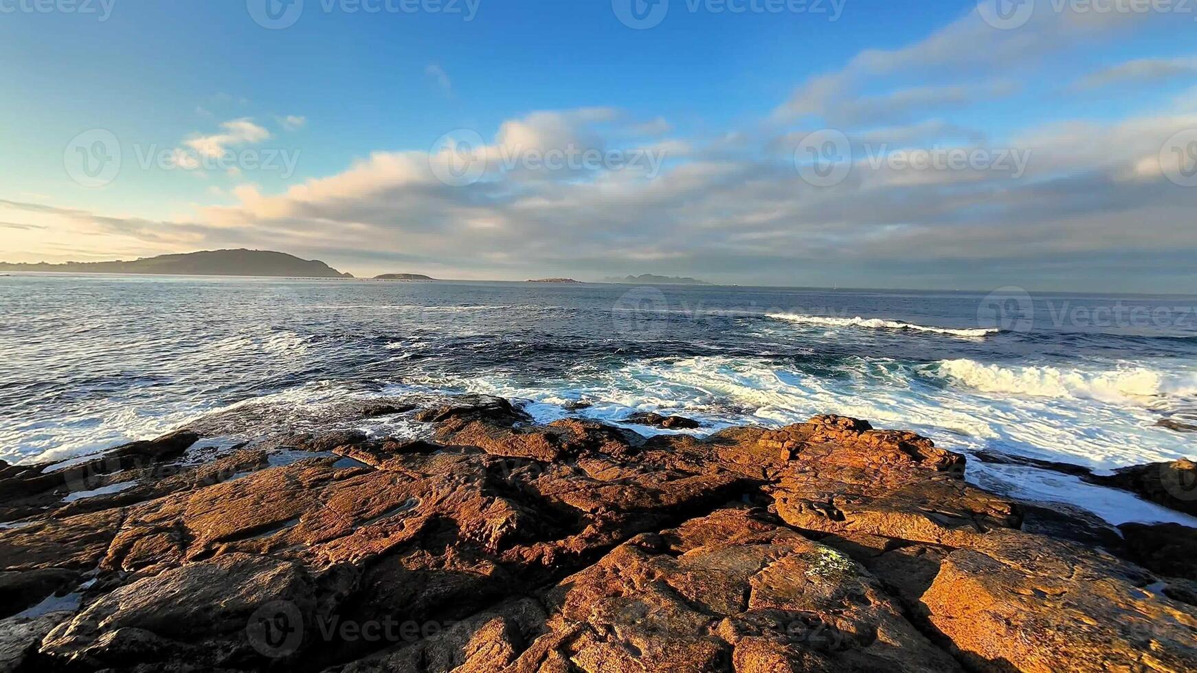 A breathtaking view showcasing the waves fiercely crashing on rugged rocks during a vibrant sunrise by the sea photo