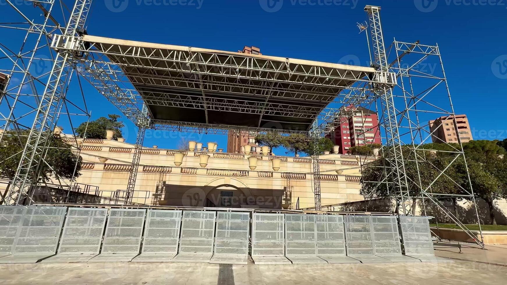 A stunning outdoor stage setup with security barriers in a lively urban environment under a clear blue sky photo