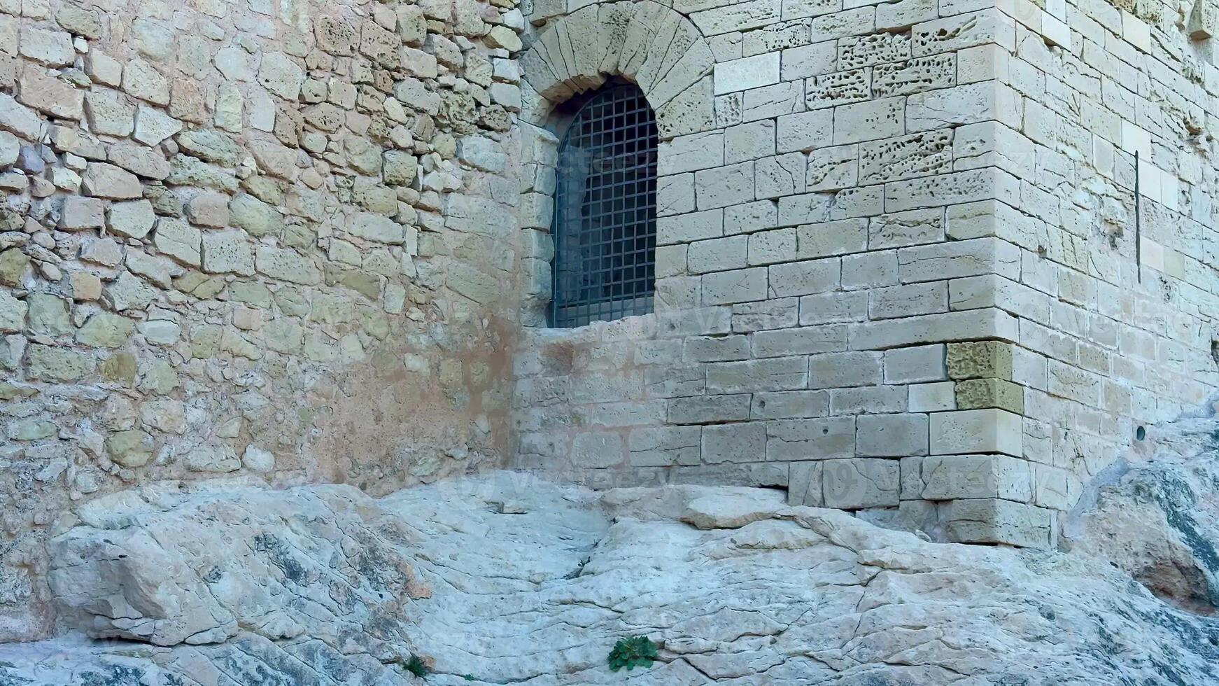 A close-up of an ancient stone building featuring a grated window, showcasing historic architecture. photo