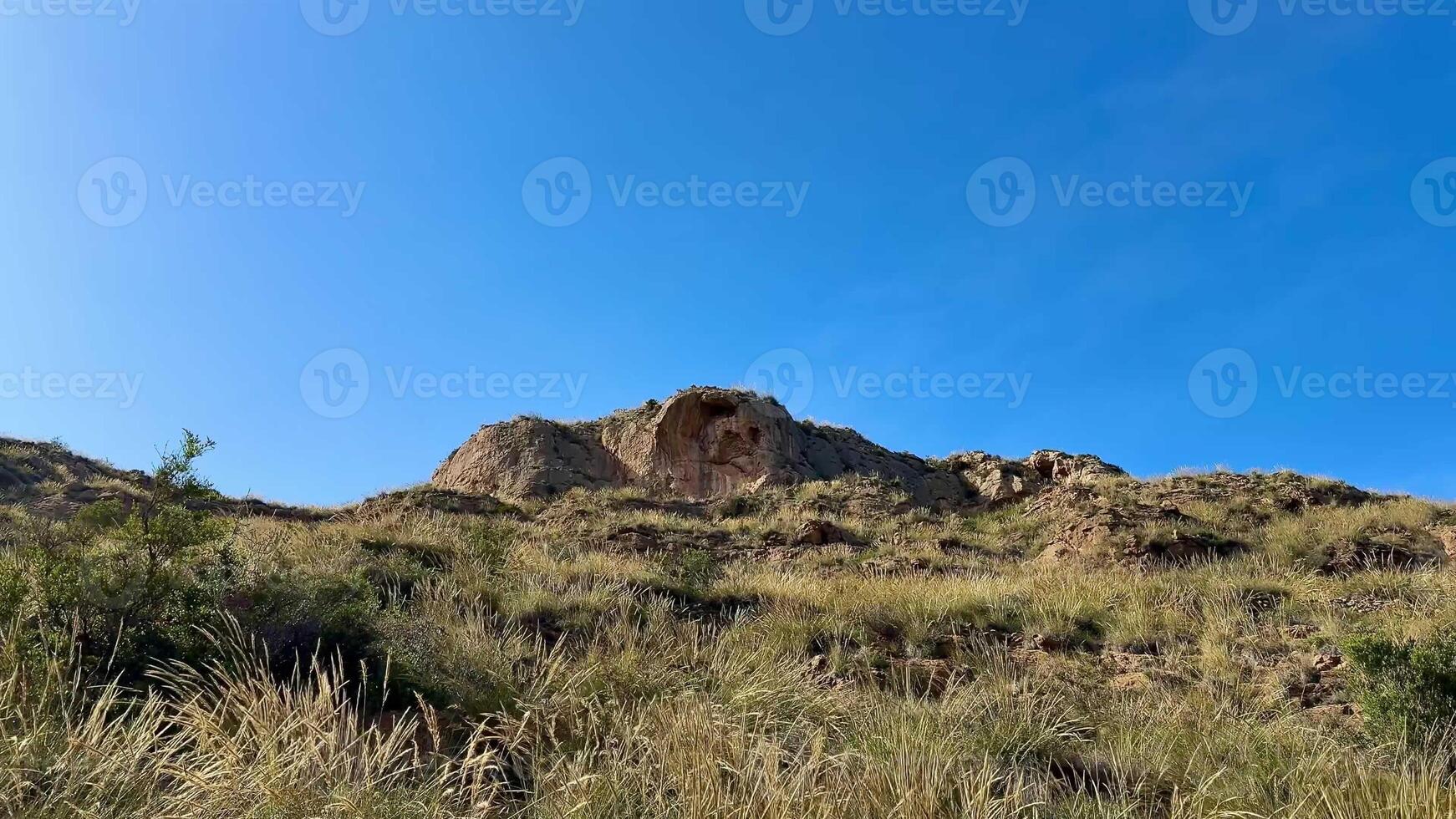 The breathtaking view of rocky hills adorned with golden grass stretches out beautifully beneath a clear blue sky photo