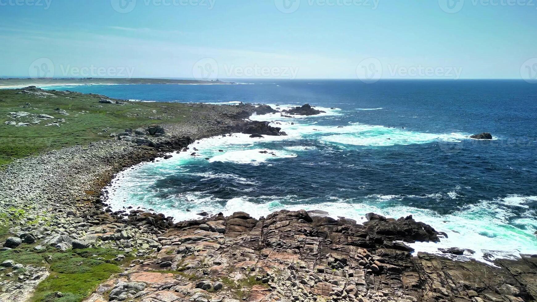 The breathtaking view of the ocean waves crashing energetically against the rocky coastline under clear blue skies photo