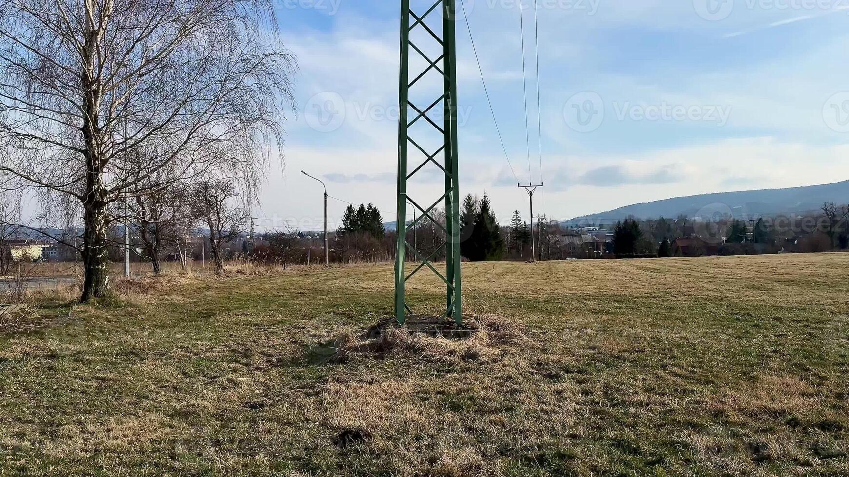 A tall electricity transmission tower rises prominently in an expansive open field that is surrounded by nature photo