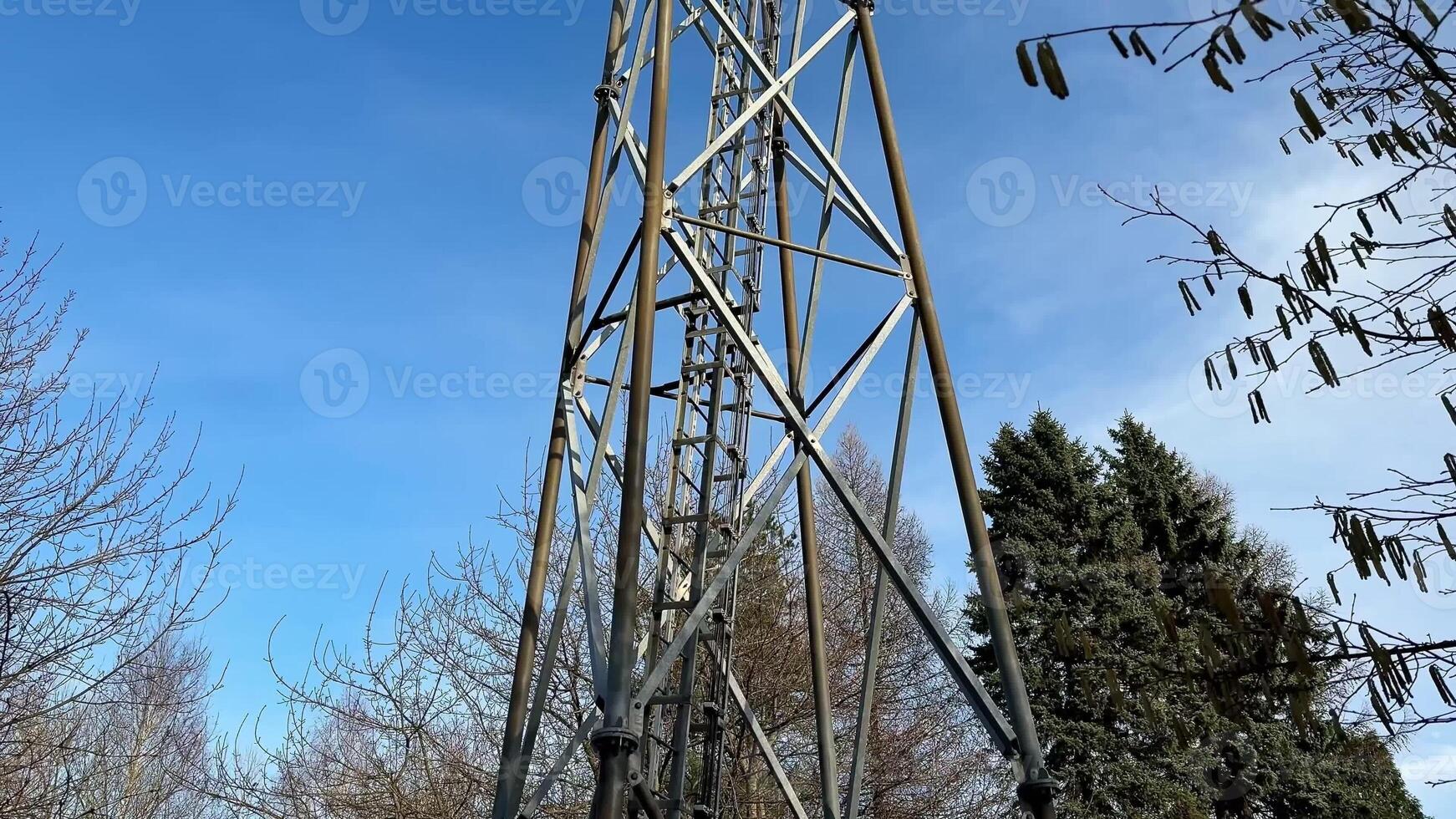 A tall and impressive communication tower is surrounded by lush green trees under a beautiful clear blue sky photo