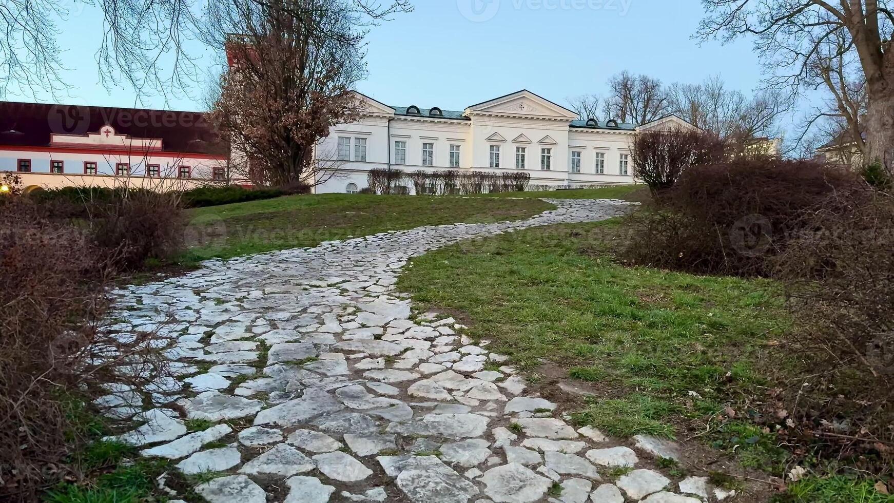 A scenic stone pathway weaves through lush greenery, guiding visitors towards a charming and historic estate photo