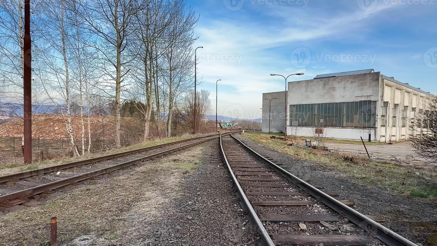 A beautifully serene view of an abandoned and overgrown railway track located next to an old industrial building photo