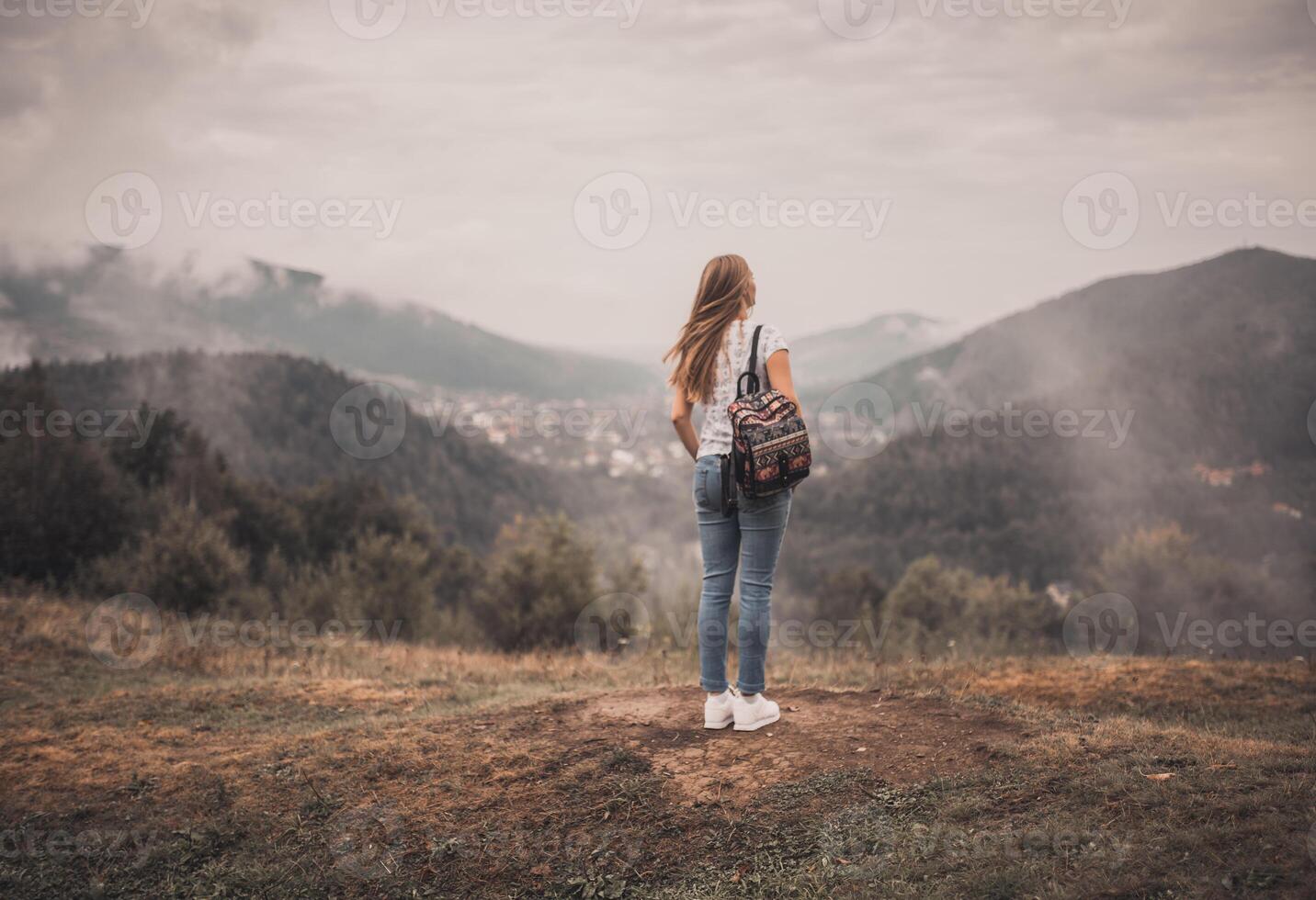 woman standing alone with backpack near mountains photo