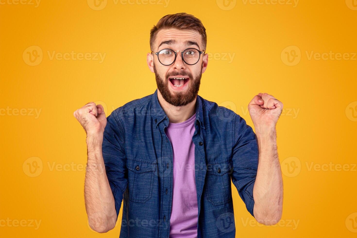Winner and success concept. Excited young guy making YES gesture with clenched fists on orange studio background. Excited Caucasian man shouting OMG, overjoyed with big win photo