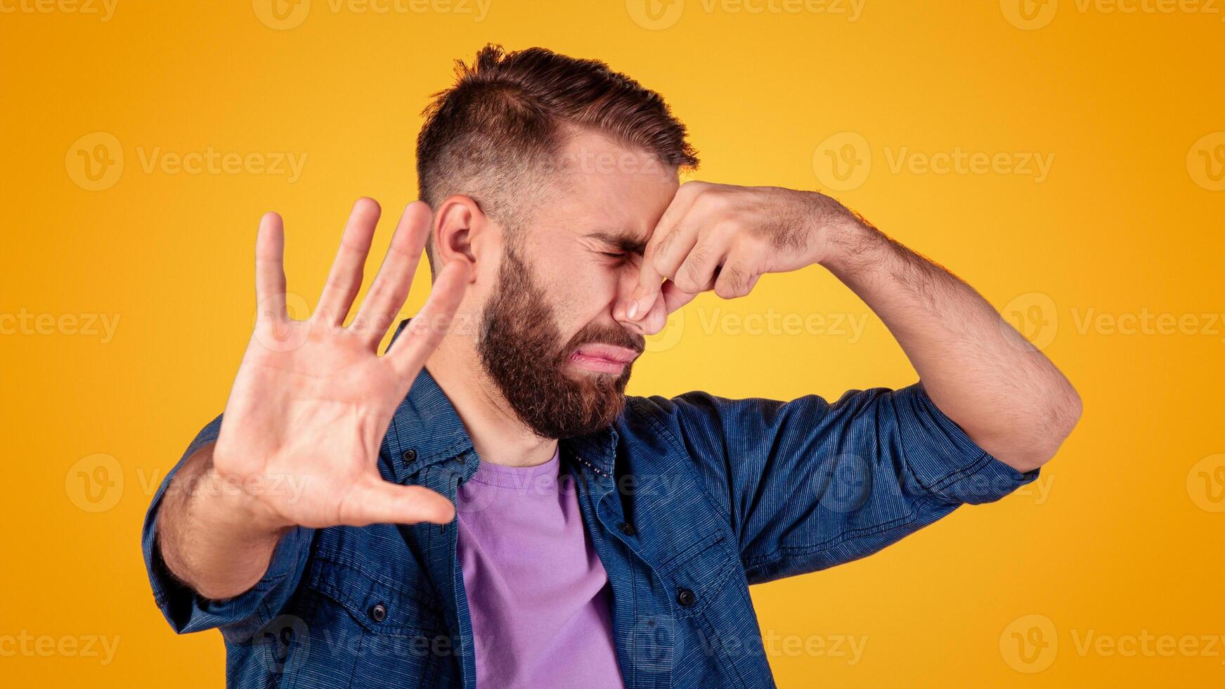 Terrible smell concept. Millennial hipster guy closing his nose and gesturing STOP, feeling disgusted on grey studio background. Young man repulsed by unpleasant odor or stinky perfume photo