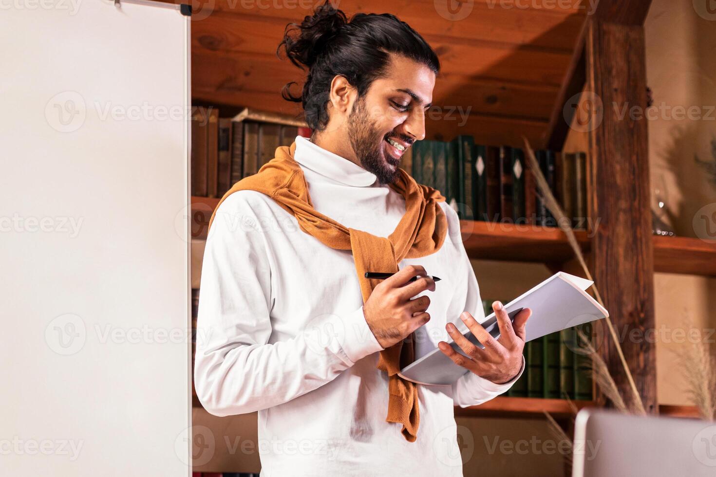 Online Teaching Concept. Indian Teacher Guy Having Web Class Explaining English Language Rules To Webcam Standing Near Blackboard At Home. Distance Study, Education And E-Teaching. Selective Focus photo