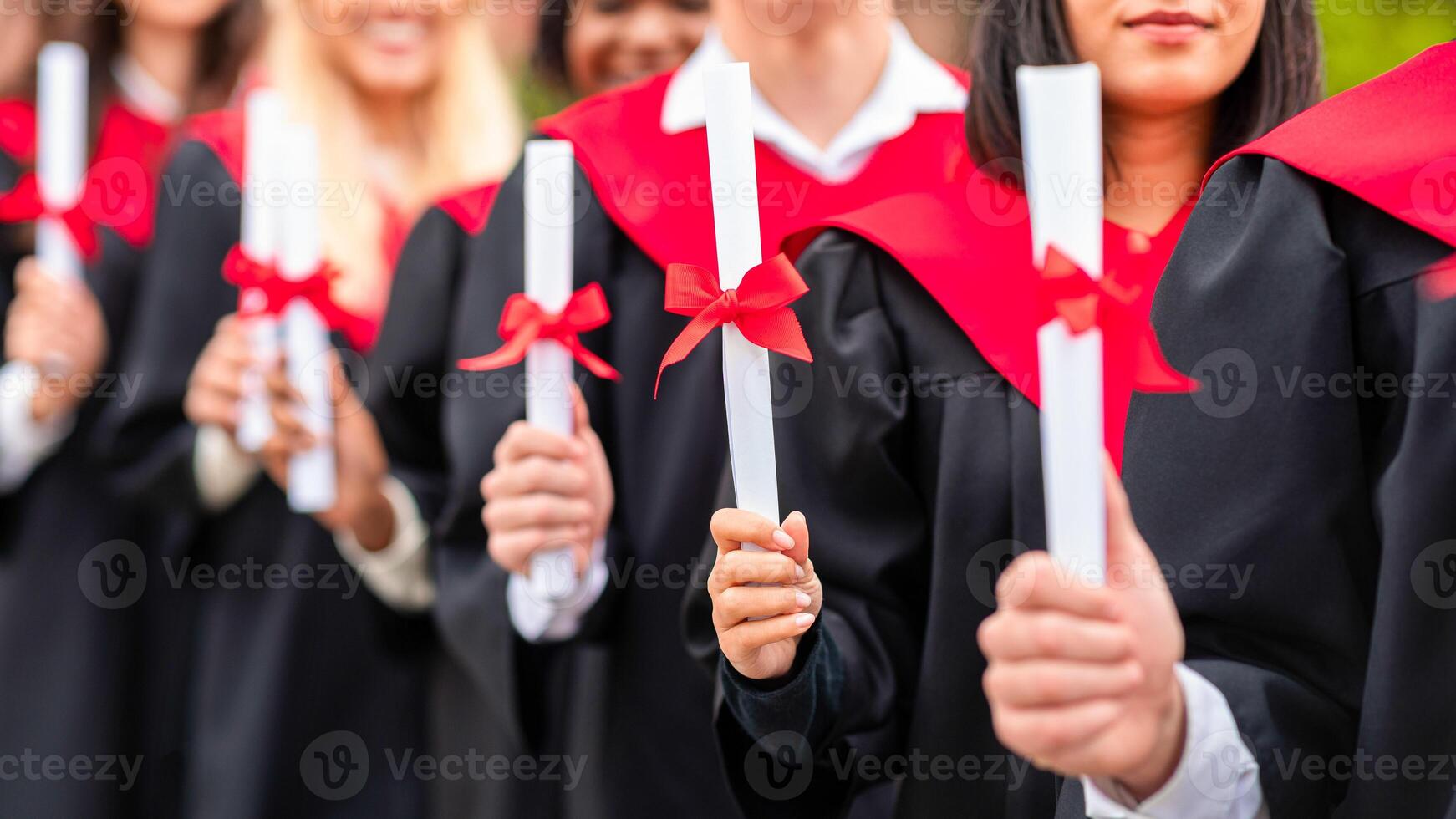 Unrecognizable international group of male and female graduators wearing graduation robes showing their diplomas, closeup. High school, university college graduation concept photo