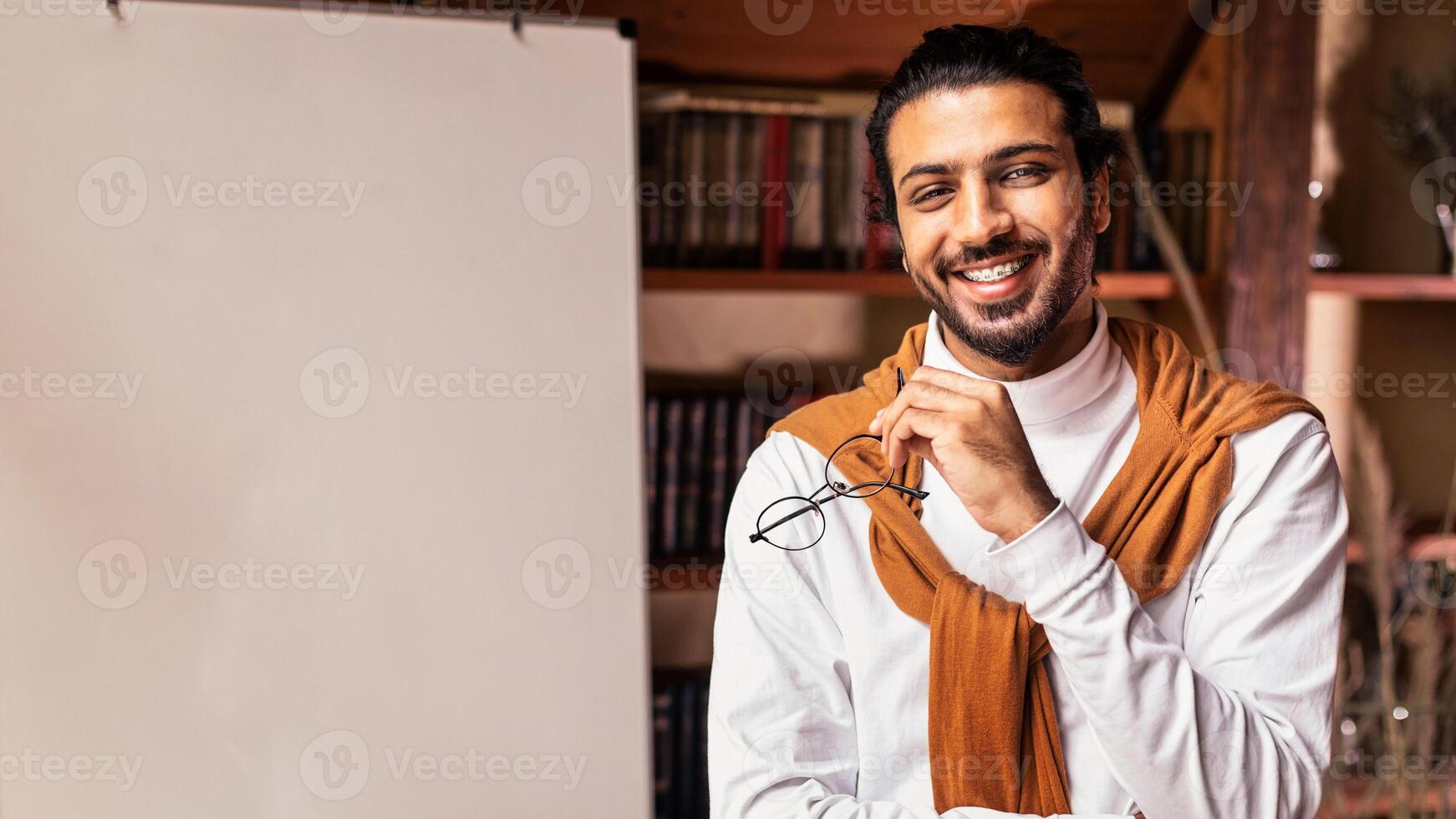 E-Learning And E-Teaching. Young Arab Male Teacher Standing Near Blackboard Teaching English Language Remotely From Home, Smiling To Camera. Distance Learning And Teaching Concept photo