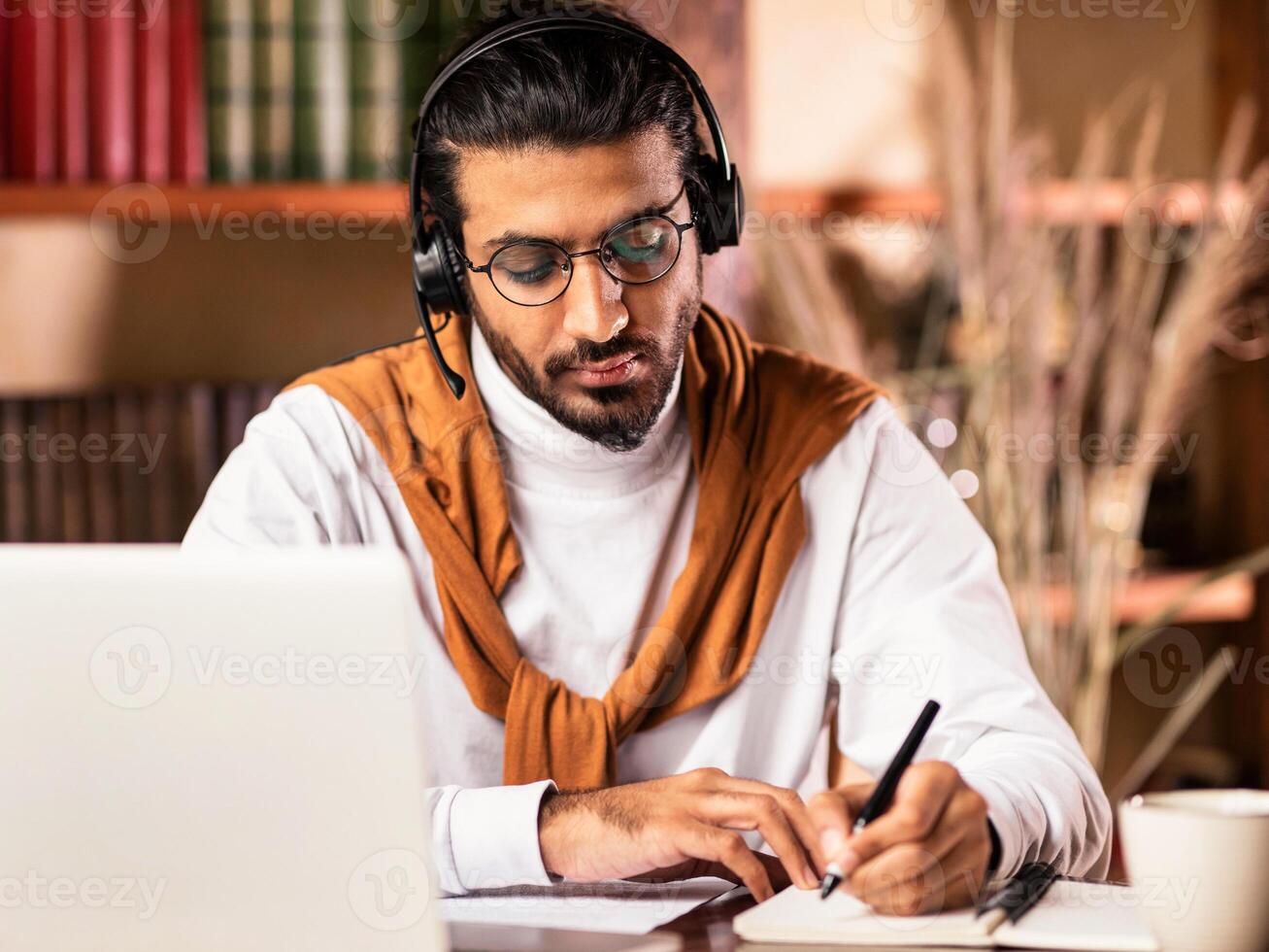 Indian Student Guy Taking Notes Learning At Laptop Doing University Homework Online Studying Remotely At Home. Distance Learning, Virtual Class And Modern Education Concept photo