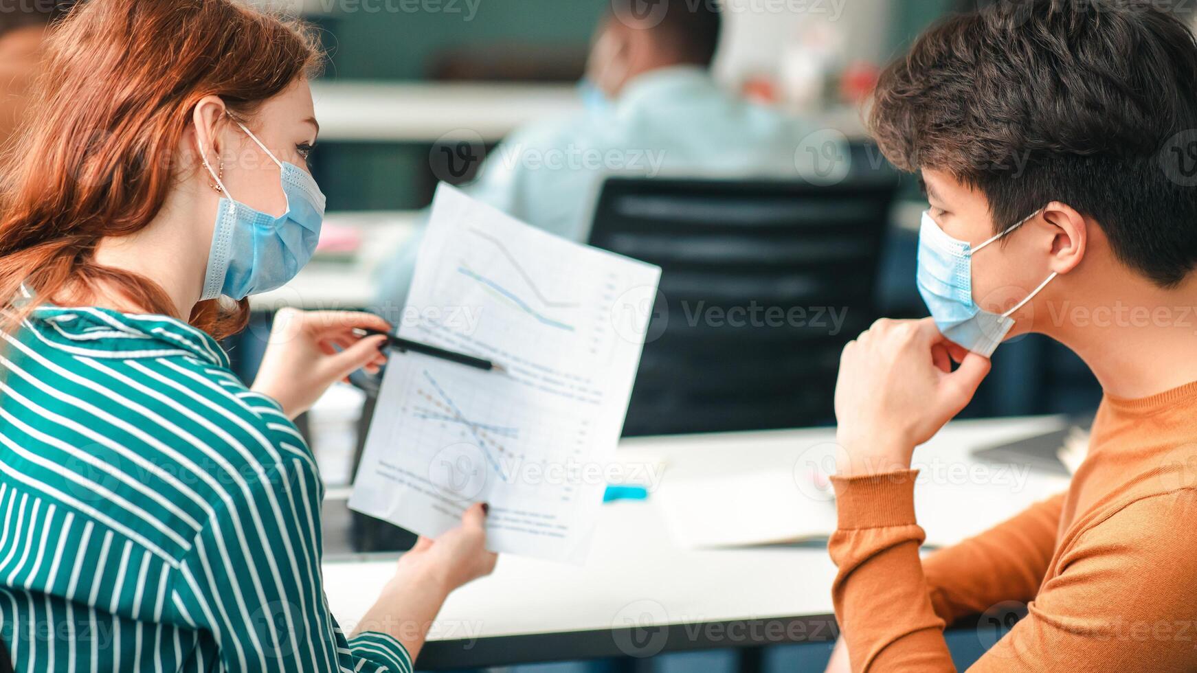 Healthcare, Education And People Concept. Group of diverse international students wearing protective medical masks and talking, discussing project, sitting at desk in lecture hall at the university photo