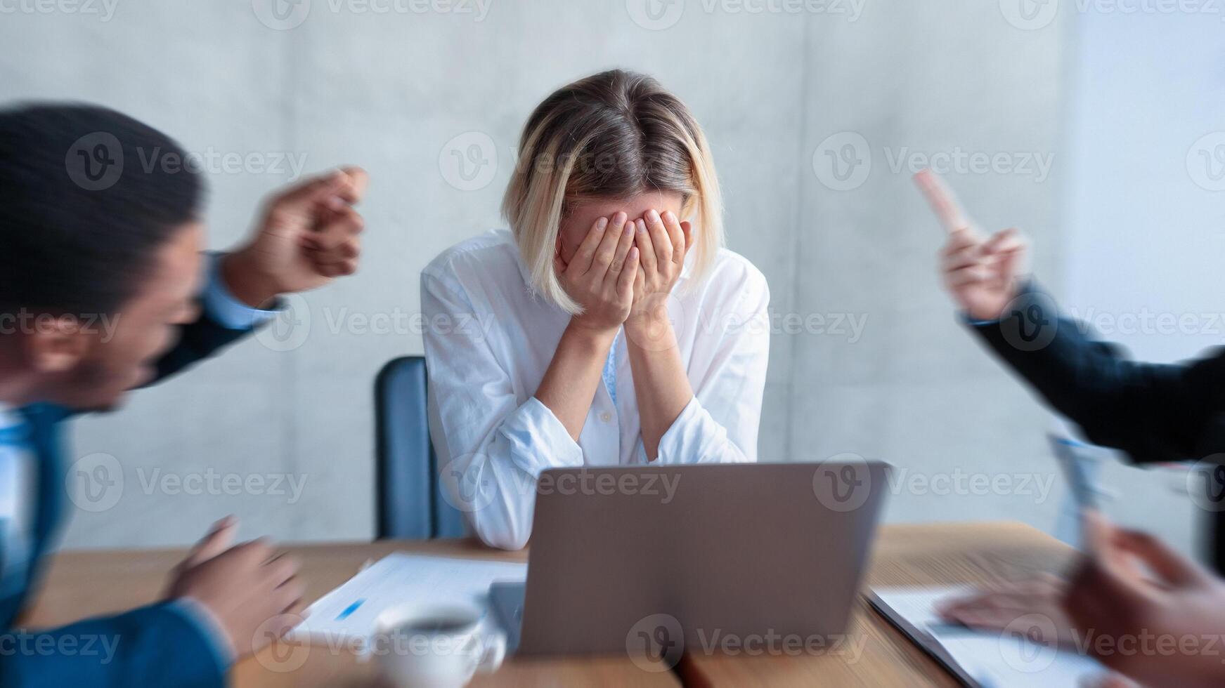Victimization At Workplace. Colleagues Shouting At Unhappy Victimized Businesswoman, While She Covering Face With Hands Sitting In Modern Office. Corporate Communication Problem And Adult Bullying photo