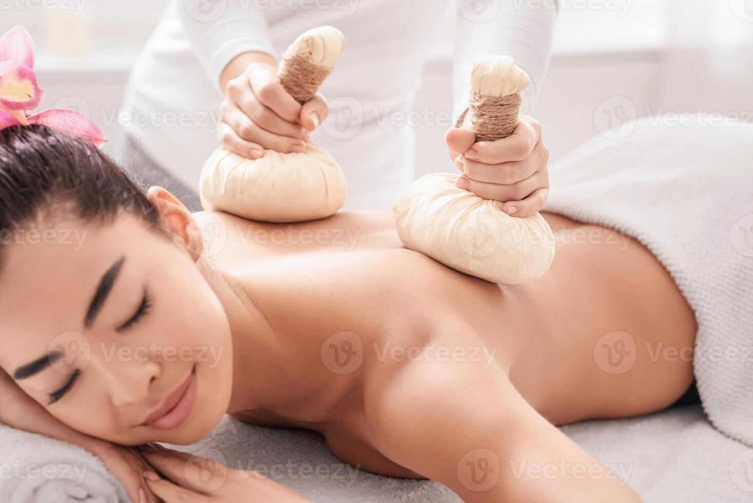 Relaxed asian woman having herbal ball compress back and shoulder massage session in spa salon, calm korean lady enjoying body treatments and self-pampering herself with beauty procedures, closeup photo