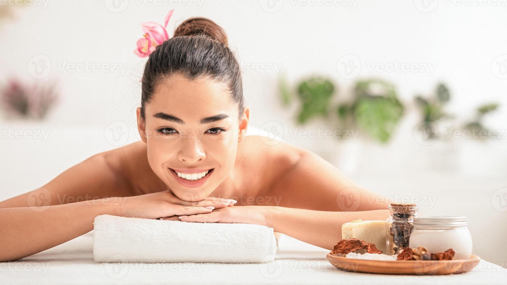 Spa Day. Portrait Of Beautiful Asian Lady Enjoying Wellness Beauty Treatments With Natural Cosmetics In Salon, Lying On Massage Table And Smiling At Camera, Having Aromatherapy Session, Free Space photo