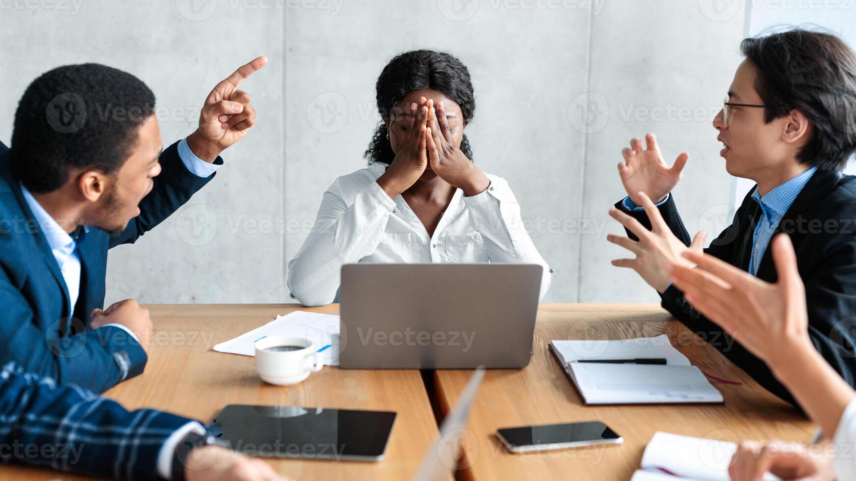 Discontented Coworkers Shouting At Unhappy Victimized Businesswoman Sitting At Table In Modern Office. Adult Bullying At Work, Conflicts And Disagreement, Business Communication Problems Concept photo