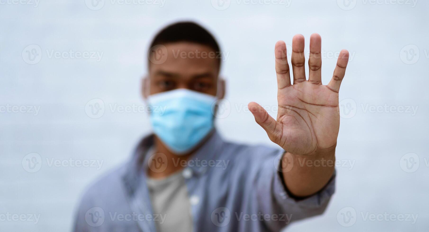 Stop Covid-19. African American Man Wearing Protective Face Mask Gesturing Stop To Camera Standing Over Gray Studio Background. Coronavirus Protection, Quarantine And Social Distance. Selective Focus photo