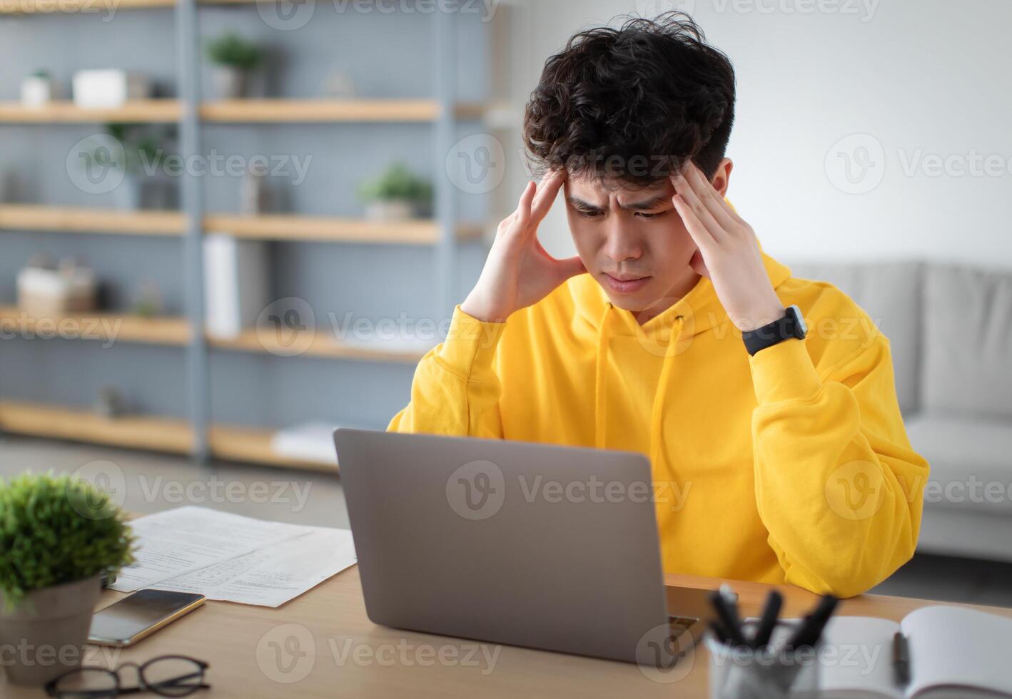 Stressed Young Asian Man Touching Temples Grabbing Head Having Problem At Workplace Sitting At Desk Looking At Laptop Screen In Home Office. Tiredness And Entrepreneurship Issues, Headache Concept photo