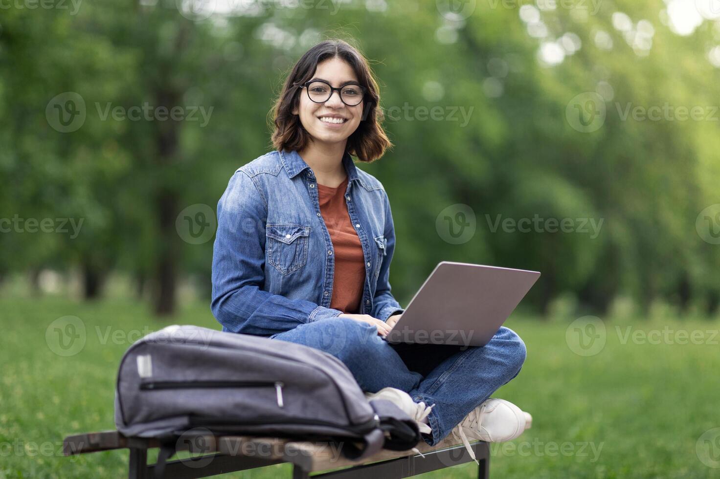 Portrait Of Happy Middle Eastern Female Student Sitting On Bench Outdoors With Laptop, Beautiful Young Arab Woman Using Computer In Park, Enjoying Online Education And Distance Learning, Copy Space photo