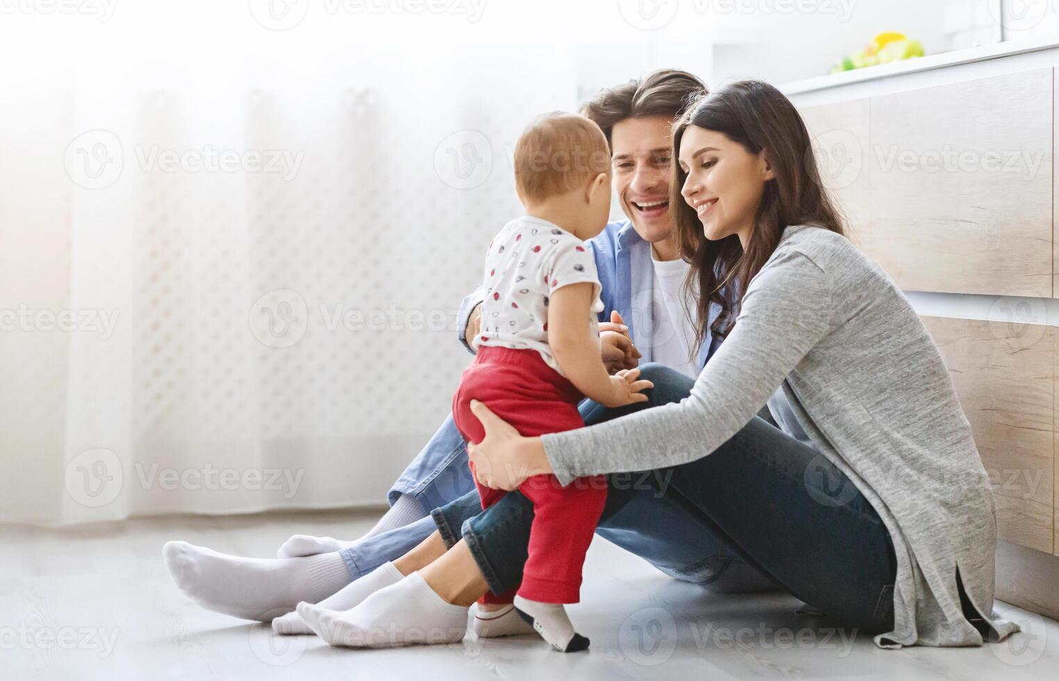 Family pastime. Cheerful mom and daddy playing with baby son on kitchen floor, free space photo