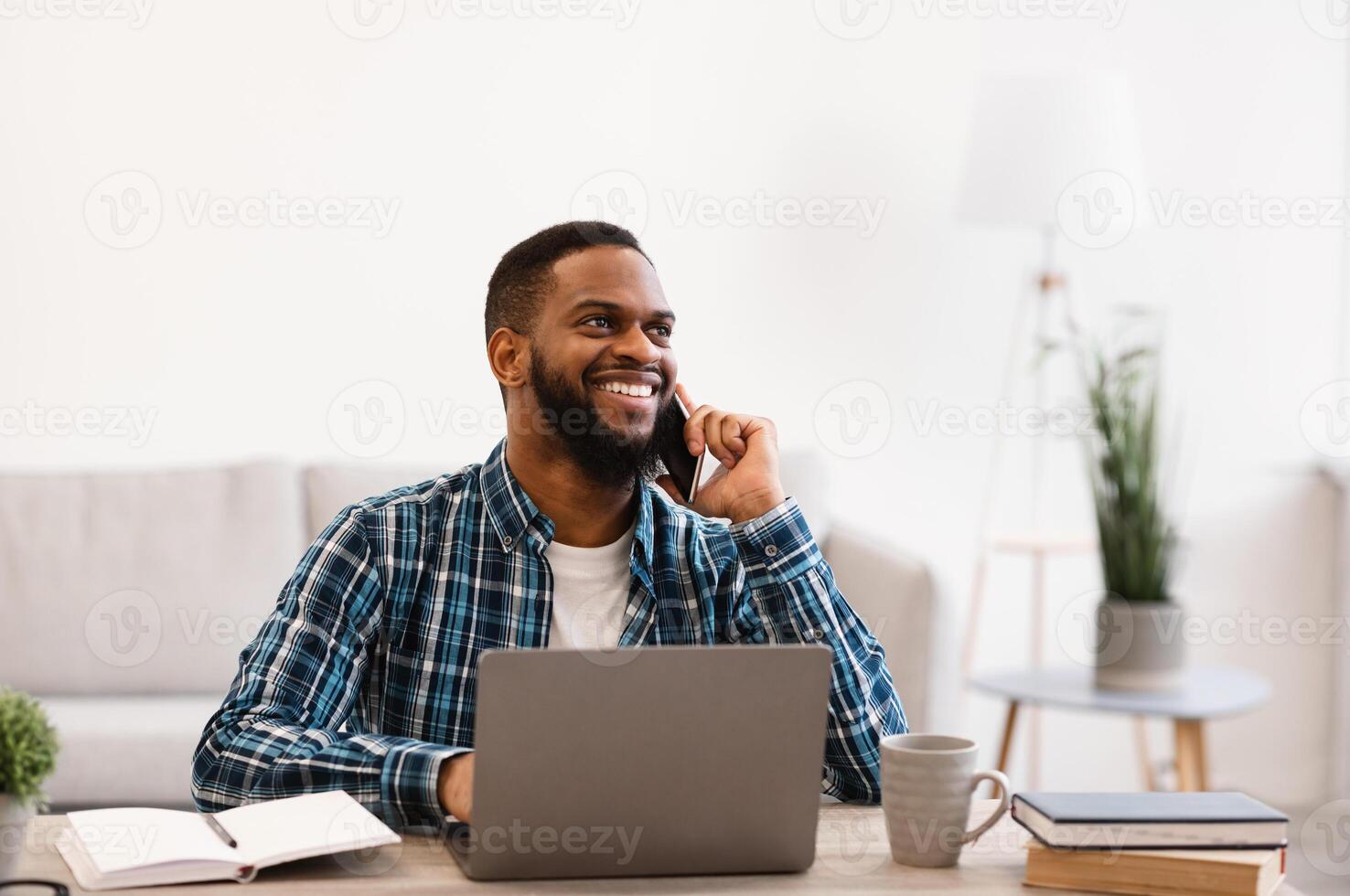 Smiling Black Businessman Talking On Phone Sitting At Workplace In Modern Office. Mobile Business Communication And Entrepreneurship. Man Having Cellphone Conversation At Work. photo