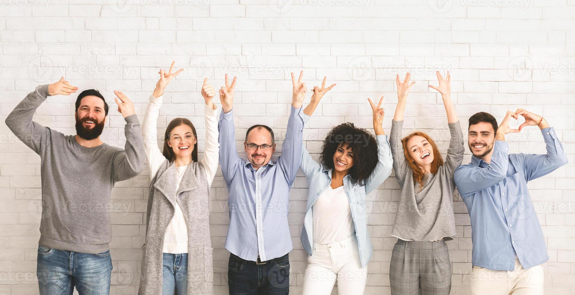 Positive Work Environment. Portrait Of Diverse Happy People Showing Funny Gestures While Posing Together Over White Brick Wall Background, Panorama photo