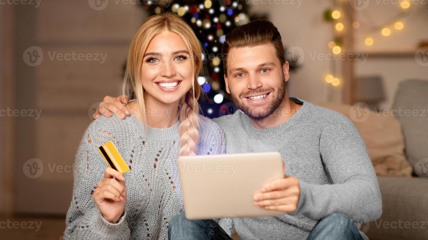 Happy family husband and wife shopping online, using digital tablet and credit card, xmas atmosphere at home. Happy young family purchasing online on pad, using Christmas discounts, copy space photo