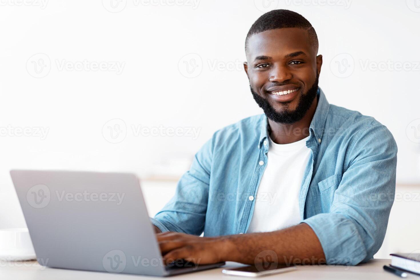 Portrait Of Happy Successful Black Freelancer Guy Posing At Desk With Laptop, Positive Millenial African American Man Smiling At Camera While Working Online On Computer In Home Office, Free Space photo