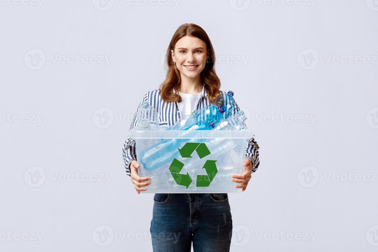Waste Reuse. Cheerful Young Woman Carrying Container With Plastic Bottles For Recycling And Smiling At Camera, Happy Eco-Activist Sorting Garbage For Recycle, Standing On Grey Background photo