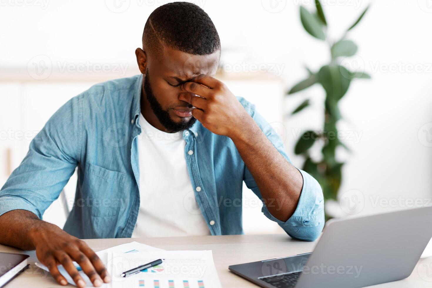 Portrait Of Stressed Black Businessman At Workplace In Office, Depressed Millennial African American Entrepreneur Sitting At Desk With Laptop And Documents, Suffering Problems At Work, Closeup Shot photo