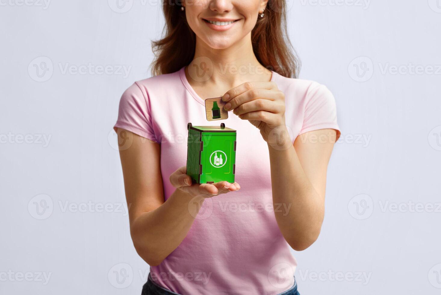 Conceptual Image For Waste Sorting. Woman Putting Card With Drinking Glass Icon Into Small Wooden Toy Garbage Container, Unrecognizable Lady Standing Over Light Background In Studio, Free Space photo