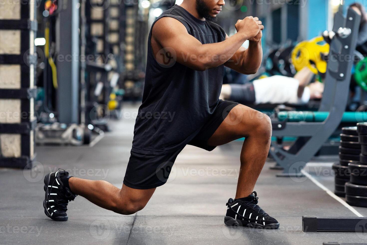 Black guy sportsman doing squats in modern gym, african american muscular young man bodybuilder doing lunges, working on legs muscles, panorama with copy space, side view photo