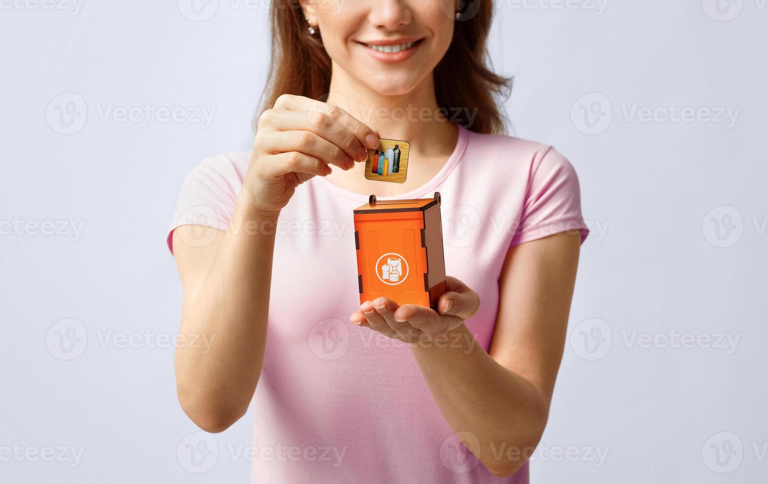 Garbage Sorting Conceptual Image With Lady Putting Card With Drawn Plastic Bottles Icon Into Small Wooden Toy Trash Container, Unrecognizable Lady Standing Over Light Background In Studio, Copy Space photo