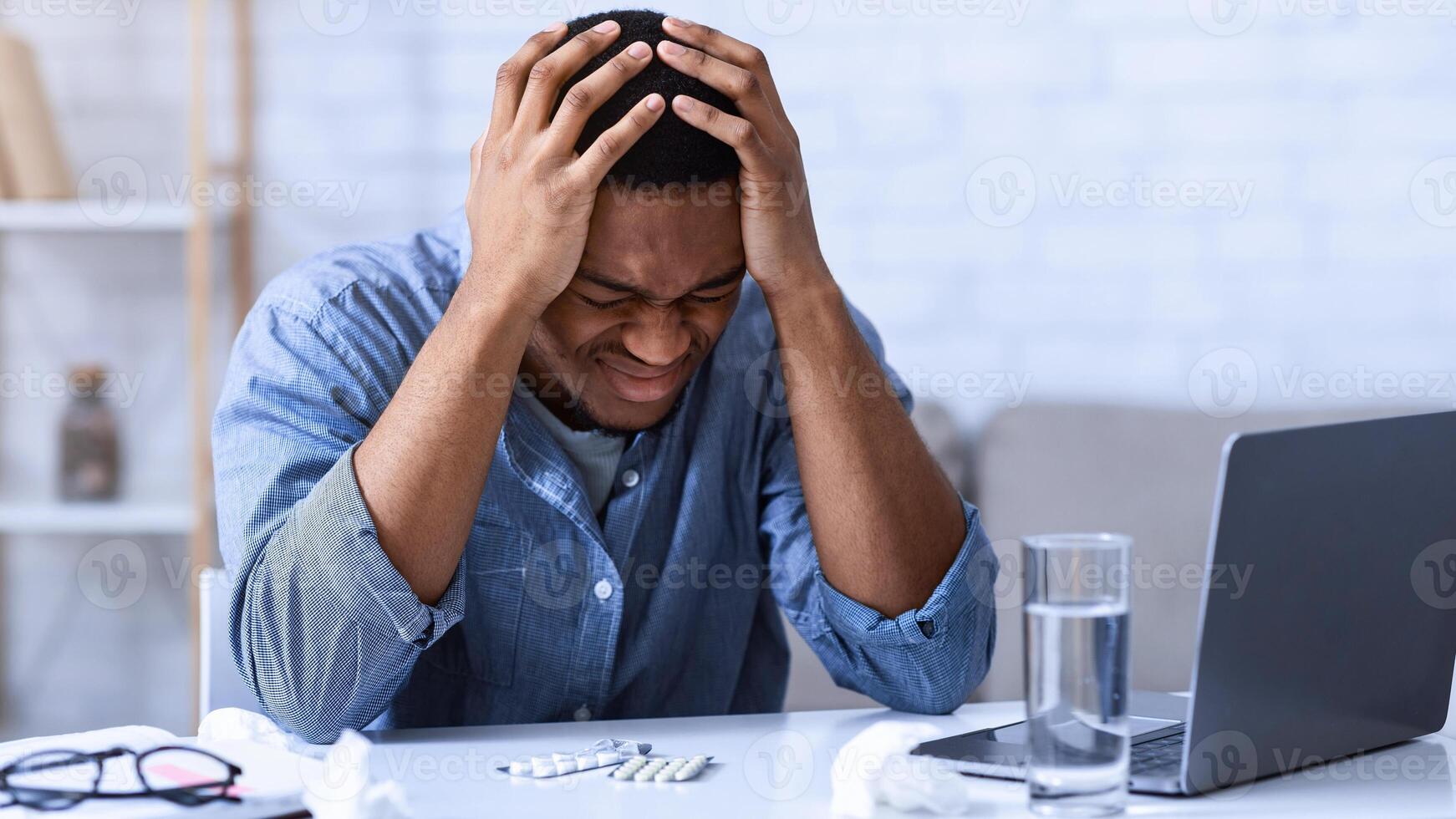 Black Man Suffering From Headache Touching Head Sitting At Workplace In Office. Unhappy African American Guy Having Migraine Feeling Bad During Work. Painful Severe Head Ache Concept. photo