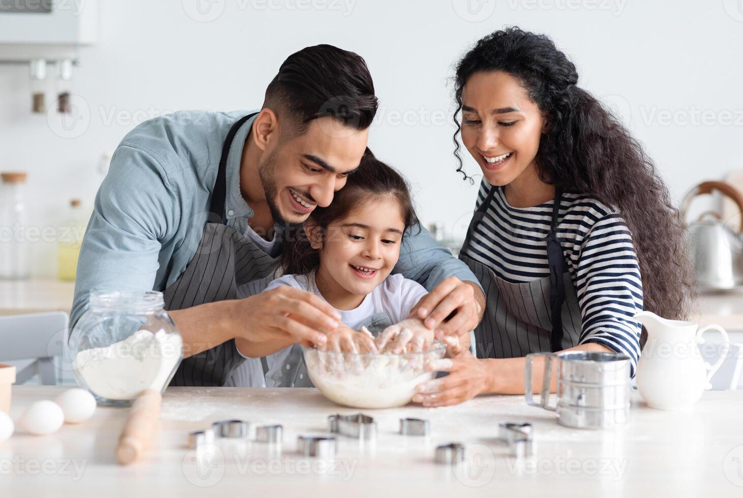 Cute arab family baking pastry together at kicthen, copy space. Joyful middle-eastern father, mother and little daughter making dough for home-made cookies. Domestic family lifestyle concept photo