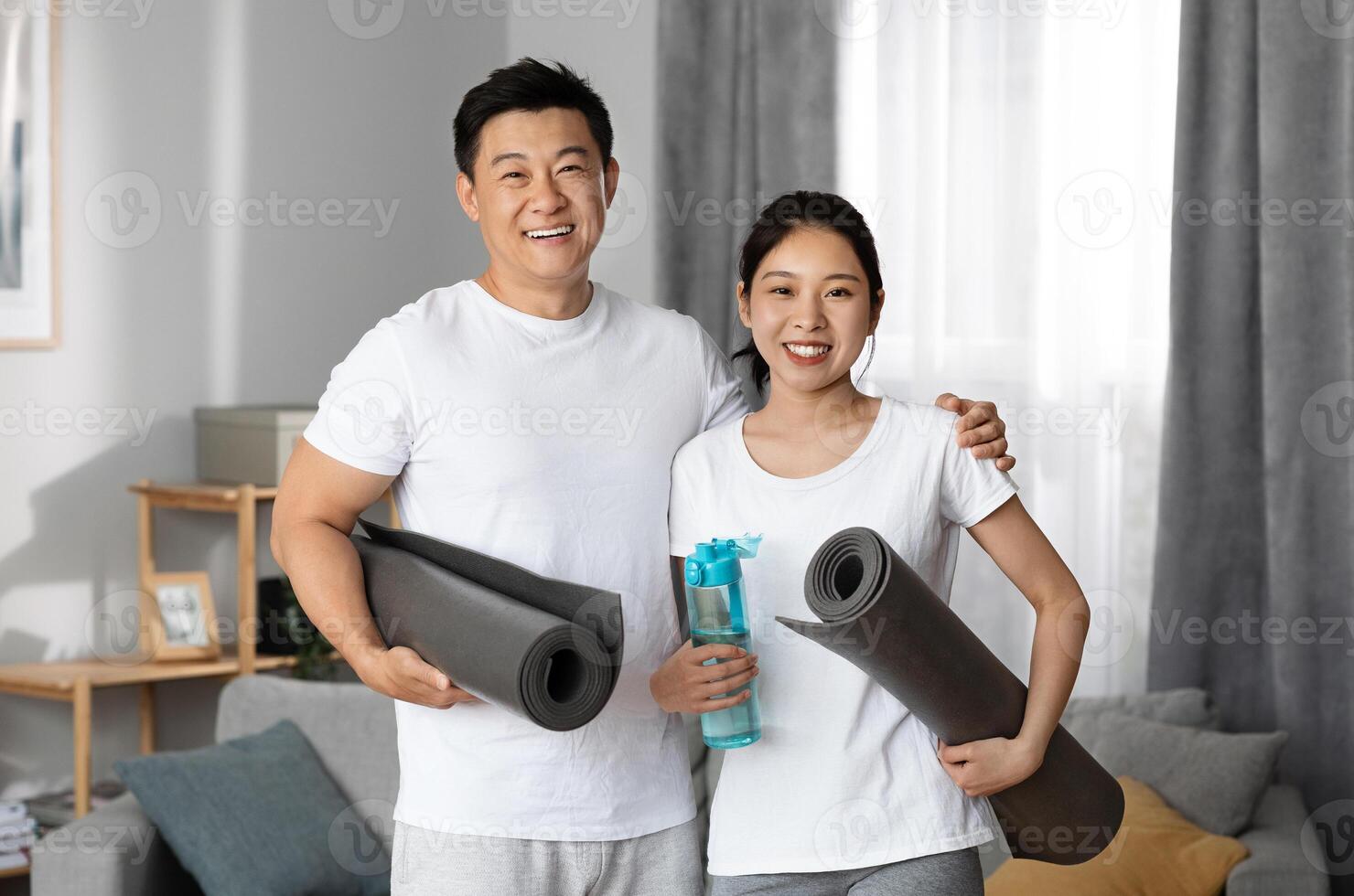 Positive asian couple going to gym together, happy korean man and woman in sportswear holding fitness mats and bottle of water, exercising at home, having morning workout, copy space photo