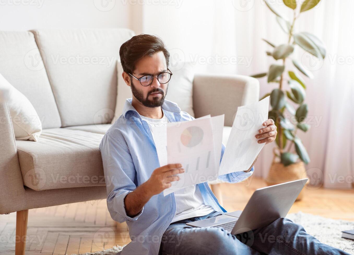 Busy Young Arab Entrepreneur Checking Papers And Using Laptop Computer At Home, Eastern Businessman Reading Financial Reports, Working Remotely, Enjoying Distance Job Opportunities, Free Space photo