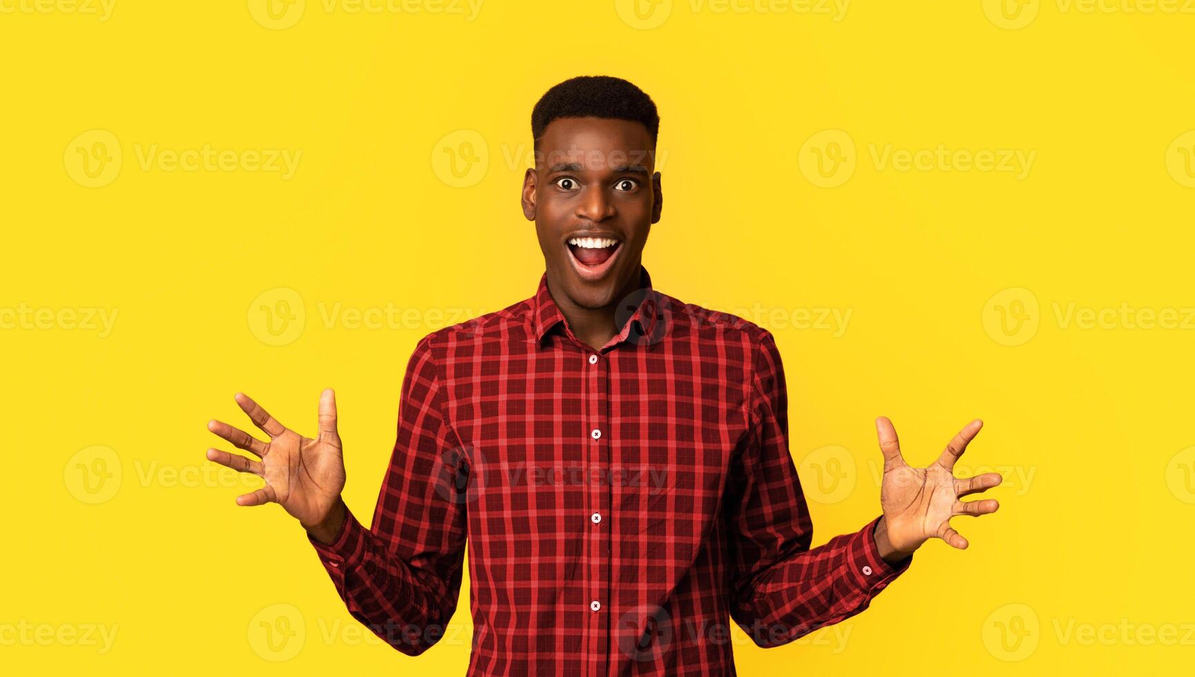 Portrait Of Overjoyed African American Guy Raising Hands In Excitement, Amazed Black Millennial Man Emotionally Reacting To Good News Or Offer, Standing Isolated Over Yellow Background, Copy Space photo