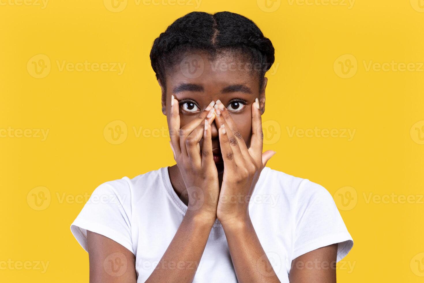 Shy African American Young Woman Looking At Camera Through Fingers Covering Face Standing Posing On Yellow Studio Background. I Don't Want To See This, Insecurity And Shyness Concept photo