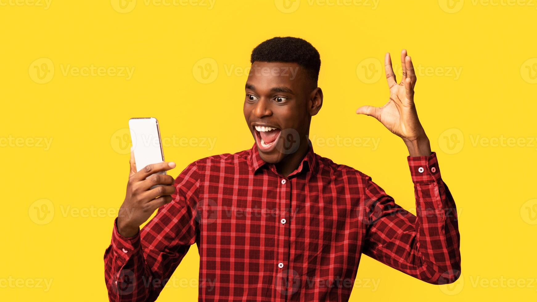 Online Win. Overjoyed African American Guy Looking At Smartphone Screen With Excitement And Raising Hand, Emotionally Reacting To Good News, Standing Isolated Over Yellow Background, Copy Space photo