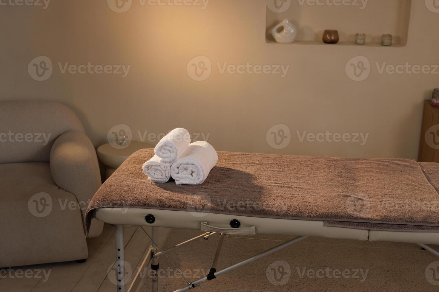 Minimalist spa interior with a clean massage table topped with neatly rolled white towels in a calming environment ready for a wellness treatment session. photo